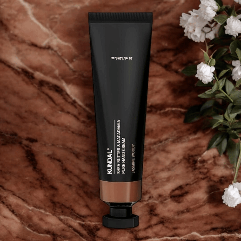 KUNDAL Shea Butter & Macadamia Pure Hand Cream Jasmine Woody placerad på marmor med blommor – närande handkräm som vårdar torra händer och ger en elegant jasmine woody-doft.