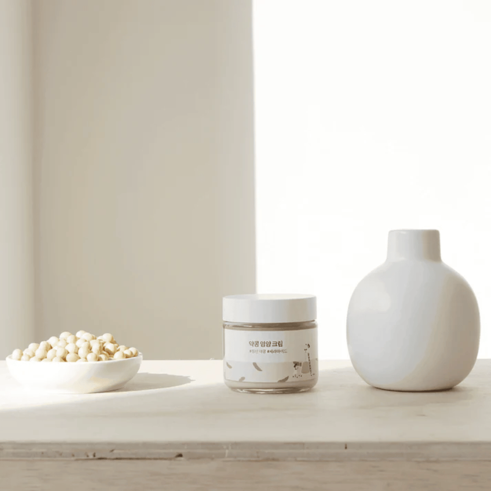Mixsoon Soybean Nourishing Cream står på ett träbord bredvid en vas och sojabönor. En minimalistisk, återfuktande kräm med naturliga ingredienser.