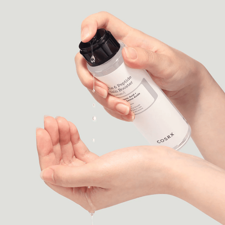 Händer som häller ut hudvårdsprodukt från en transparent flaska med texten "The Peptide Skin Booster".
