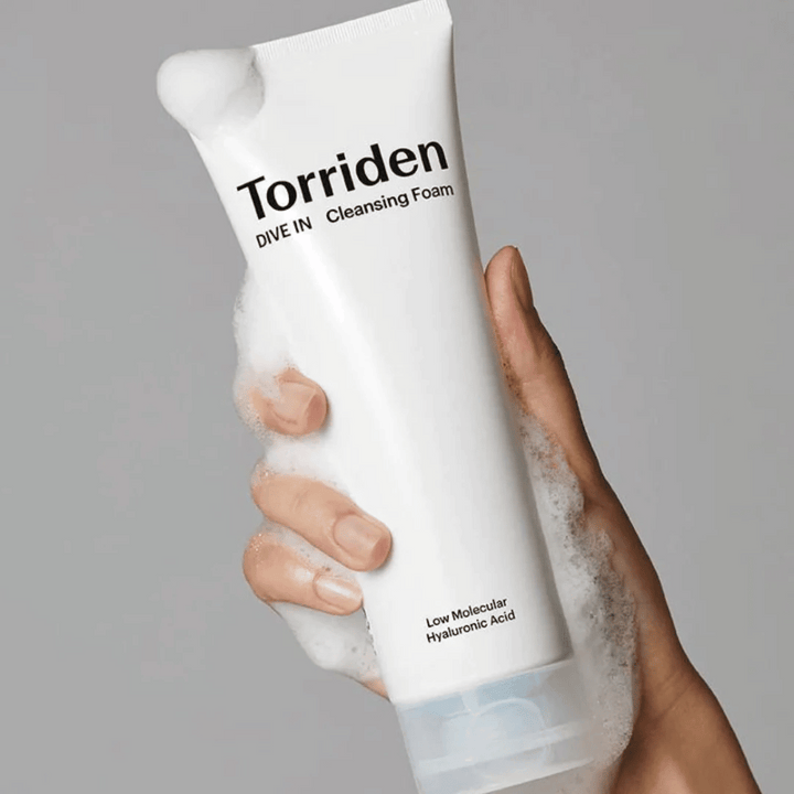 En hand som håller i en tub pH-balanserad Torriden DIVE-IN Low Molecular Hyaluronic Acid Cleansing Foam 150ml.
