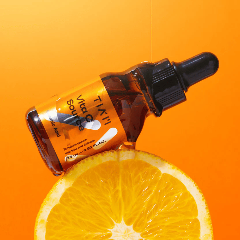 TIA'M Vita C Source-flaska placerad mot en apelsin och en orange bakgrund som symboliserar C-vitaminets fräschör och antioxidativa effekt.