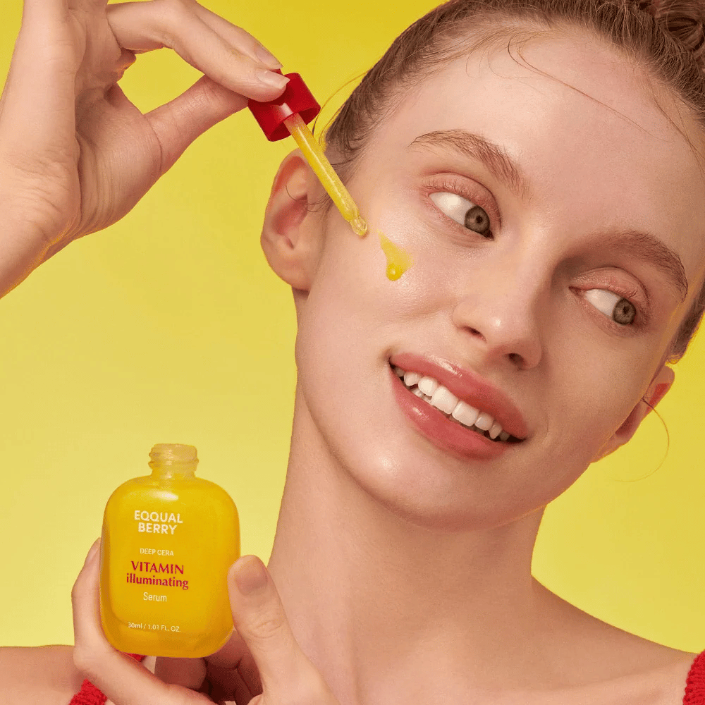 Leende kvinna applicerar Equal Berry Vitamin Illuminating Serum med en pipett. Frisk och strålande hud mot en livlig gul bakgrund som matchar serumets färg.