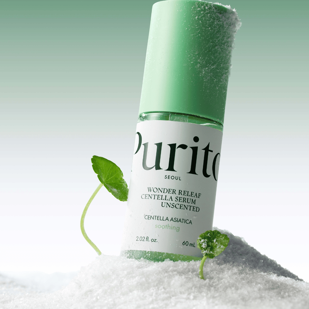 Flaska med Purito Centella Serum ligger i snö, gröna blad syns, mot en mjuk grön bakgrund.
