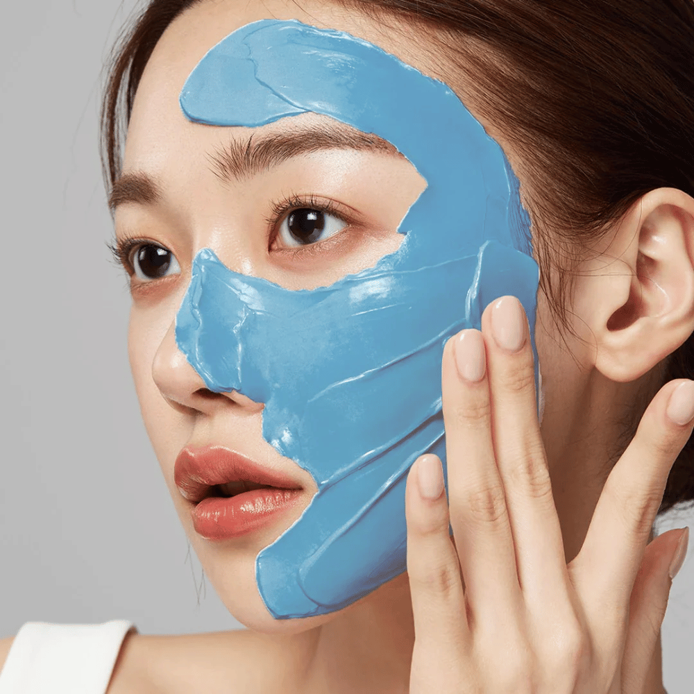 Modell med blå ansiktsmask från Medicube, täcker T-zonen för porvård.