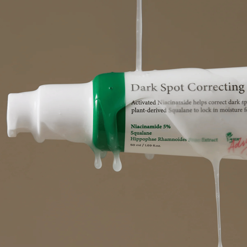 Närbild på en pumpflaska av Axis-Y Dark Spot Correcting Glow Serum med vit förpackning och grön kork, täckt av rinnande genomskinlig vätska.