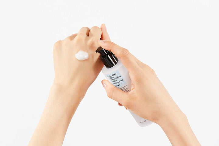 En kvinnas hand håller i en flaska COSRX Oil Free Ultra Moisturizing Lotion med Björksav 100 ml på en vit bakgrund.