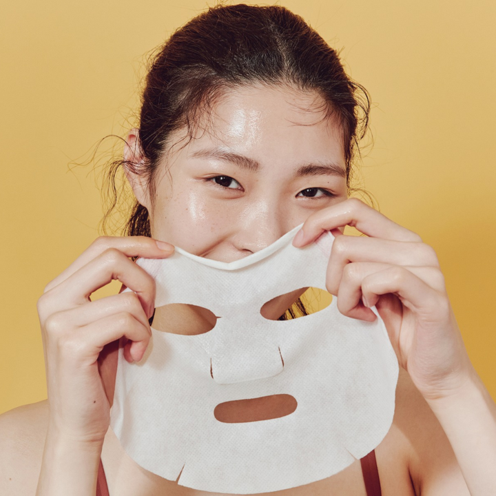 En kvinna håller en COSRX Full Fit Propolis Nourishing Magnet Sheet Mask över ansiktet för återfuktning och skadad hud.