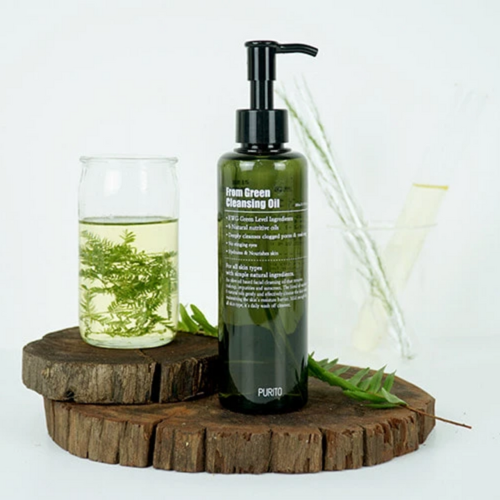 En flaska PURITO From Green Cleansing Oil 200ml sitter på toppen av en trästubb.