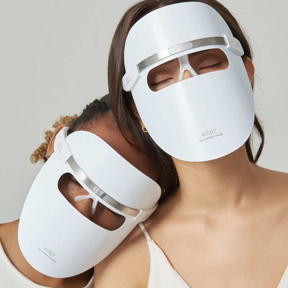 Två kvinnor som bär vita masker demonstrerar ECLAIR LED Therapy Mask för hudtonen förbättringar.