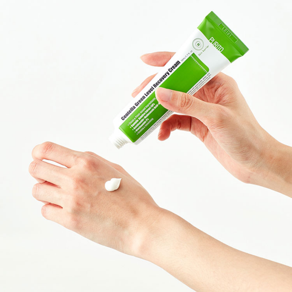 En hand håller i en tub PURITO Centella Green Level Recovery Cream 50ml på en vit bakgrund.