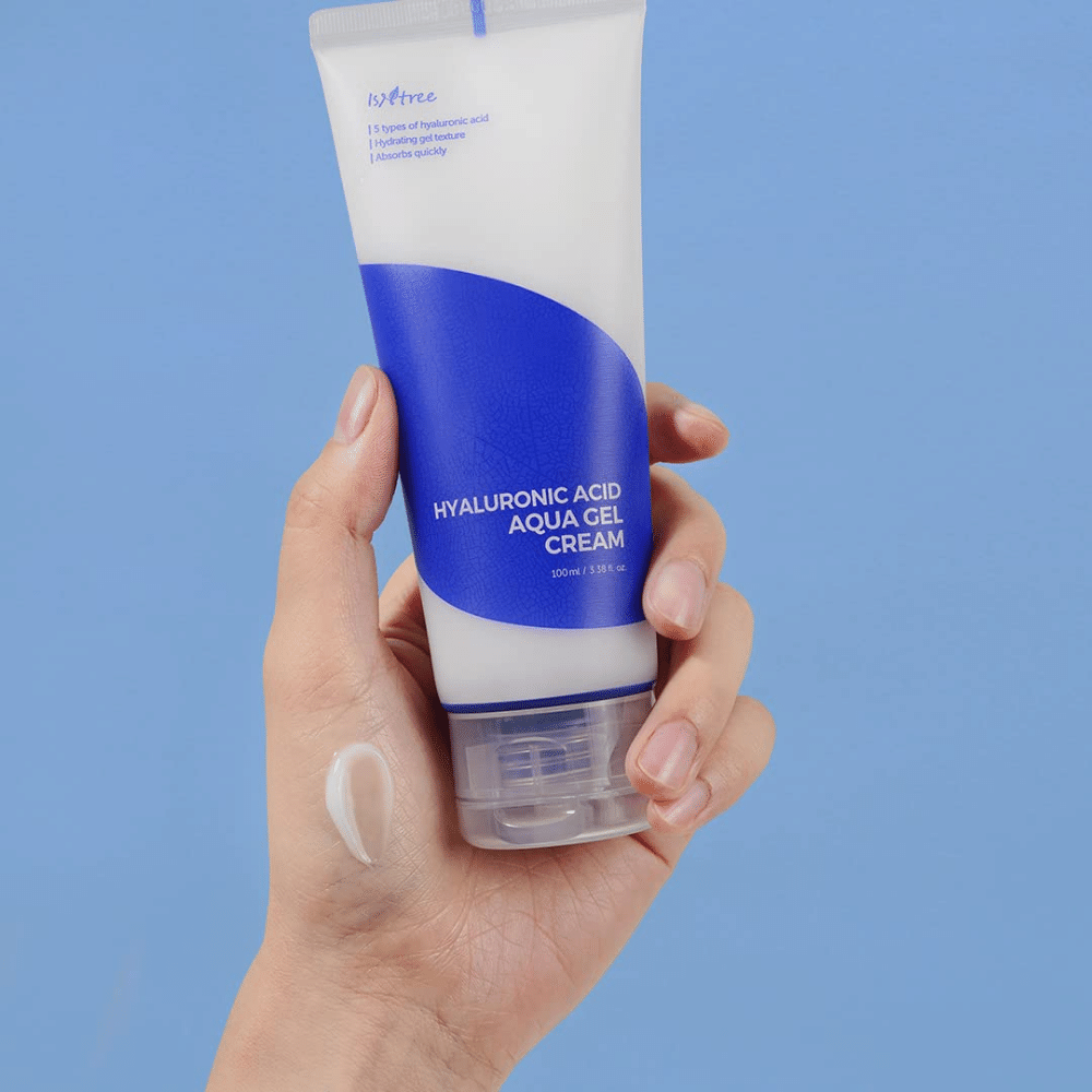 En hand som håller i en tub Isntree Hyaluronic Acid Aqua Gel Cream 100ml på en blå bakgrund.