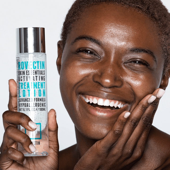 En svart kvinna som håller upp en flaska ROVECTIN Skin Essentials Activating Treatment Lotion 180 ml ansiktsrengöring.